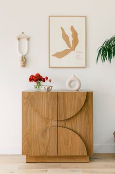 a wooden cabinet sitting in front of a painting on the wall next to a potted plant