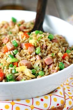 a bowl filled with rice and vegetables on top of a colorful table cloth next to a wooden spoon