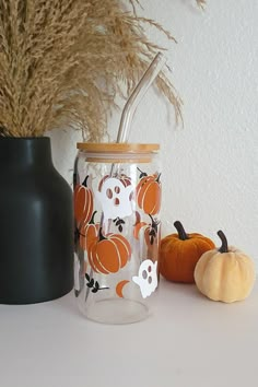 two pumpkins are sitting on a table next to a glass jar with a straw in it