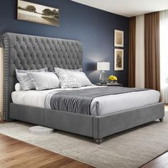 a bedroom with blue walls and white bedding in the center is a gray tufted upholstered bed