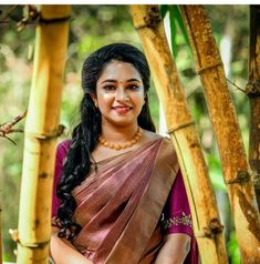 a woman in a sari standing next to some bamboo trees and looking at the camera