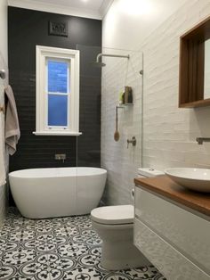 a white bath tub sitting next to a toilet under a bathroom window in a bathroom