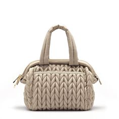 a beige handbag with braiding on the front and shoulder strap, sitting upright against a white background