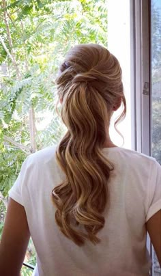 a woman is looking out the window with her long hair pulled into a half - up ponytail