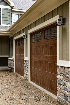 two brown garage doors are on the side of a house in front of a stone wall