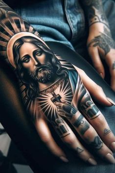 a man's hand with tattoos on it and a jesus tattoo on the palm