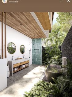 a bathroom with two sinks and mirrors on the wall, surrounded by greenery in front of it