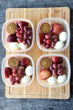 four plastic containers filled with food on top of a wooden cutting board