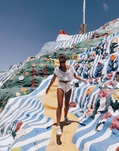 a woman is walking down a colorfully painted hill with flowers and trees on it