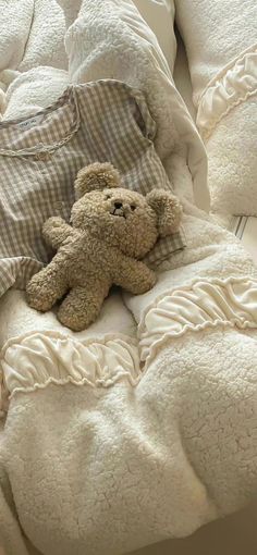 a teddy bear laying on top of a bed covered in white sheets and blanketes