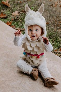 a baby in a costume sitting on the ground wearing an owl hat with ears and tail