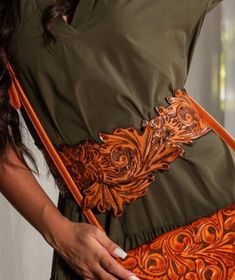 a woman is holding an orange and brown handbag in her right hand while wearing a green dress