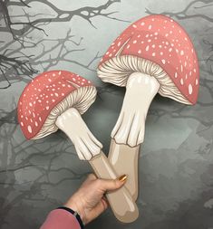 a person holding up two mushrooms in front of a wall with tree branches on it