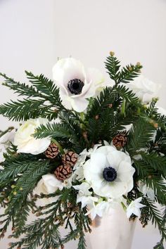 an arrangement of white flowers and pine cones in a vase