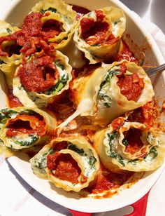 a white dish filled with stuffed shells covered in marinara sauce and spinach leaves