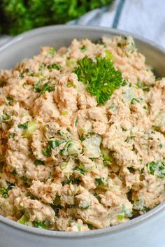 a white bowl filled with tuna salad and garnished with parsley on top