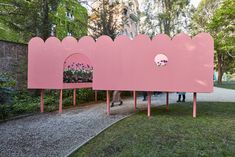 two people standing in front of a pink structure with flowers growing out of the holes