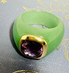 This exquisite ring embodies a harmonious blend of elegance and mystique. Crafted by artisans, the lush green Jade intricately intertwines with the regal purple Amethyst, set in a 9-carat gold setting. Each facet of this piece reflects craftsmanship, making it a timeless adornment for those who appreciate the allure of unique artisan jewelry. Green Amethyst Rings In Fine Jewelry Style, Classic Green Amethyst Ring Gift, Classic Green Amethyst Ring As Gift, Classic Green Amethyst Ring For Gift, Elegant Green Oval Amethyst Ring, Elegant Yellow Gold Ring With Natural Stones, Elegant Yellow Gold Rings With Natural Stones, Green Amethyst Ring Fine Jewelry, Exquisite Amethyst Ring With Gemstone Accents