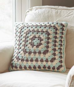 a crocheted pillow sitting on top of a white couch next to a window