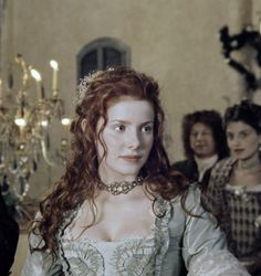 a woman with red hair wearing a white dress and sitting in front of other women