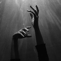 two hands reaching up into the air with sunlight streaming through them, in black and white