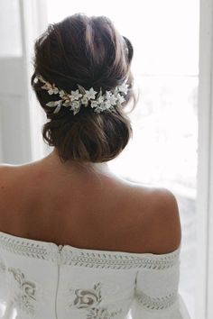 a woman wearing a white wedding dress with flowers in her hair is looking out the window