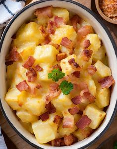 a bowl filled with potatoes and bacon on top of a wooden table next to other dishes