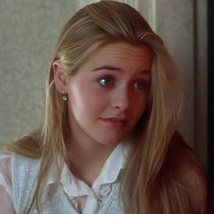 a woman with long blonde hair wearing a white shirt and silver earrings looking at the camera