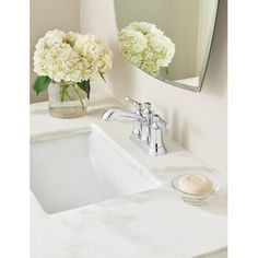 a white bathroom sink sitting under a mirror next to a vase with flowers in it