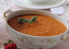 there is a bowl of soup on the table with strawberries and tea cups nearby