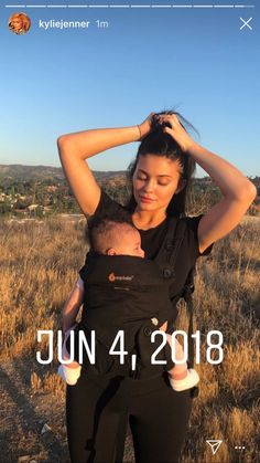 a woman holding a baby in her arms while standing on top of a grass covered field