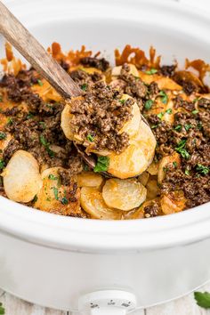 a white crock pot filled with cooked potatoes and ground beef, garnished with parsley