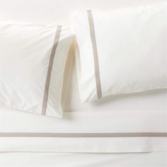 two pillow cases with white and grey trims on top of each other in a bed