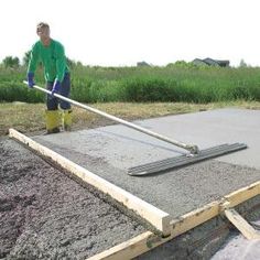 a man in green shirt and yellow boots working on cement with a large metal pole