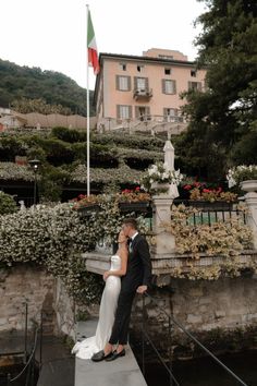 a bride and groom kissing on a bridge in front of a building with a flag