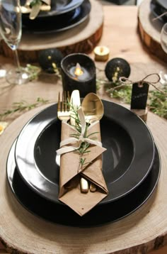 a table set with black plates and napkins, silverware and candlesticks