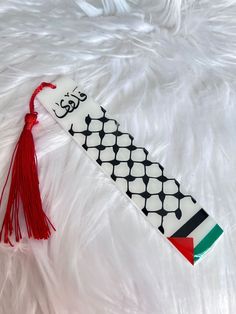 a white and black tie with a red tassel on it's end sitting on a fluffy surface