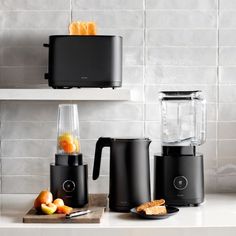 three black blenders sitting on top of a counter next to fruit and toaster