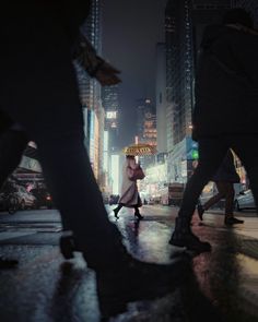 people walking in the rain with umbrellas on a city street at night, near tall buildings