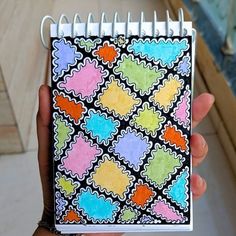 a hand holding a small notebook with colorful designs on it