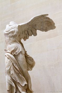 an angel statue with its wings spread out in front of a white marble wall and floor