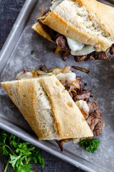 two sandwiches with meat, cheese and onions are on a metal tray next to parsley