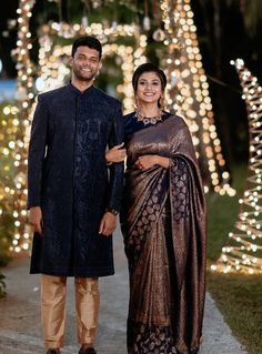 a man and woman standing next to each other in front of some trees with lights