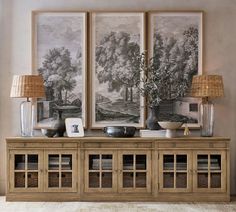 two paintings hang on the wall above a wooden cabinet with glass doors and baskets below it