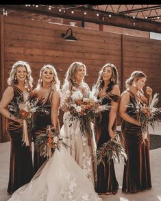 a group of women standing next to each other in front of a wooden wall holding bouquets