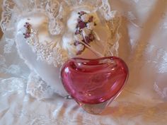 a pink glass vase sitting on top of a white lace covered tablecloth next to a heart shaped object