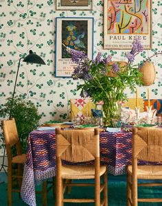 a dining room table set for four with flowers on the wall and pictures above it