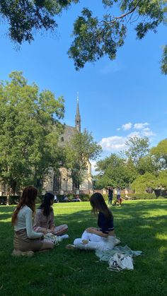 three young women sitting on the grass in front of a building with a clock tower