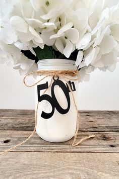 a mason jar filled with white flowers on top of a wooden table next to a string