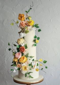 a three tiered white cake with flowers on top and green leaves around the edges